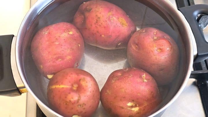 Whole red salad potatoes boiling in a large pot of salted water on the stove.