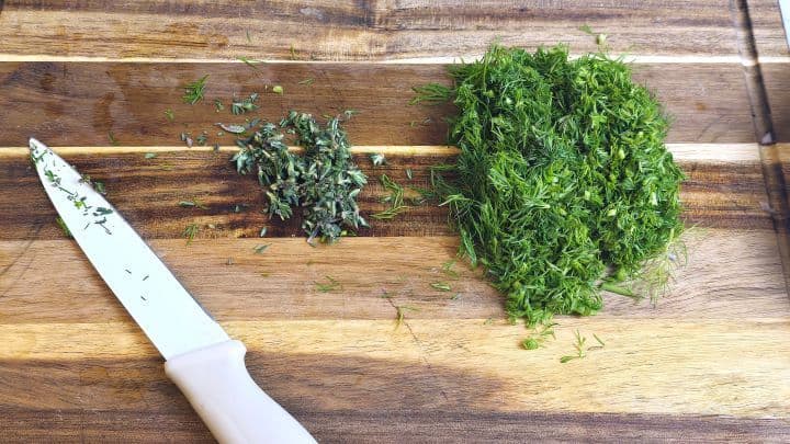 Finely chopped fresh dill and thyme herbs on a cutting board.