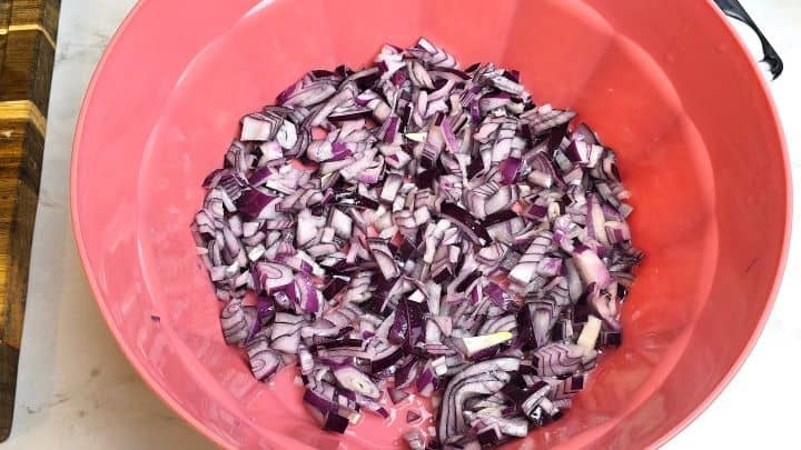 Chopped red onions tossed with sea salt and sunflower oil in a red bowl to soften.