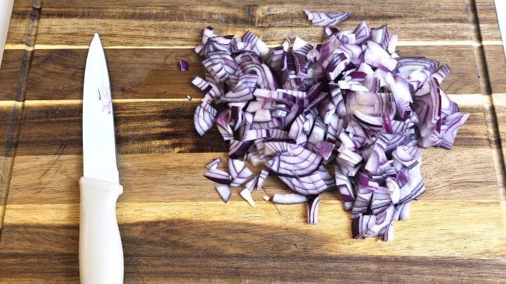 Diced red onions on a cutting board prepared for the salad base.
