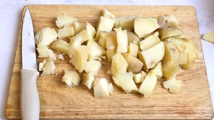 Boiled red potatoes peeled and cut into neat, bite-sized cubes on a wooden cutting board.