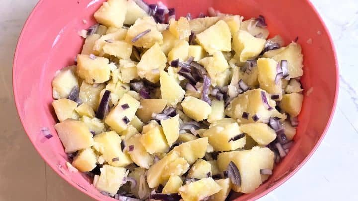 Gently combining cubed boiled potatoes and softened red onions in a large serving bowl.