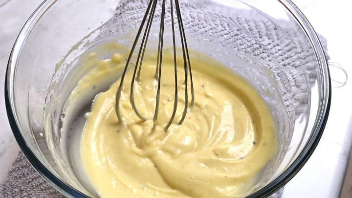 Whisking egg yolks and oil to create a thick homemade mayonnaise emulsion in a mixing bowl.