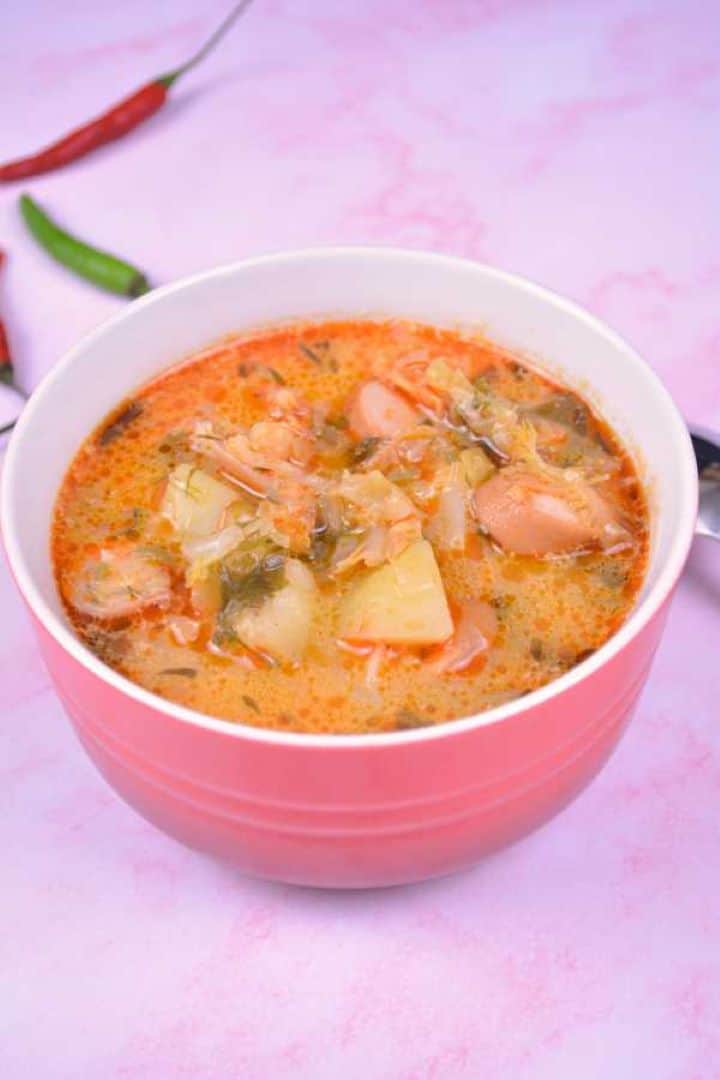 Savoy Cabbage Soup with Frankfurters Served in Red Bowl With Chilly Peppers