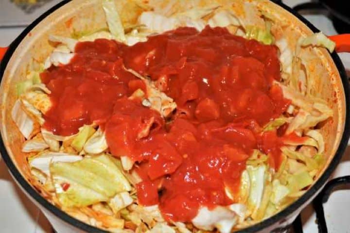 Cabbage Soup With Pork Meat-Canned Copped Tomatoes Over the Sliced Cabbage in the Pot Pouring a can of chopped tomatoes over the cabbage and pork meat in a large pot.