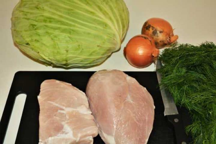 Cabbage Soup With Pork Meat-One Head Cabbage, Two Onions, Pork Meat and Dill Raw ingredients for cabbage soup with pork meat arranged on a chopping board including fresh cabbage, onions, pork shoulder, and dill.