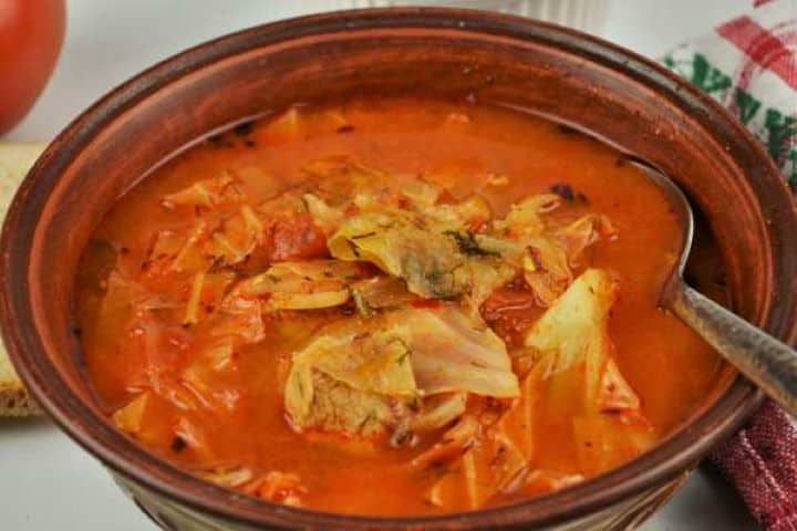 Cabbage Soup With Pork Meat-Served in Bowl With Fresh Bread A close-up of cabbage soup with pork meat in a ceramic bowl with a side of crusty sourdough bread.
