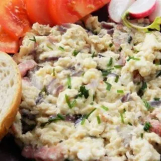 Best scrambled eggs recipe with onion, bacon and cheese, served with fresh bread, tomatoes and radishes