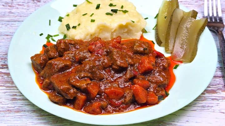 Hungarian Beef Stew Served on Plate With Mashed Potatoes and Pickled Cucumber