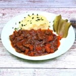 Hungarian Beef Stew Served on Plate With Mashed Potatoes and Pickled Cucumber