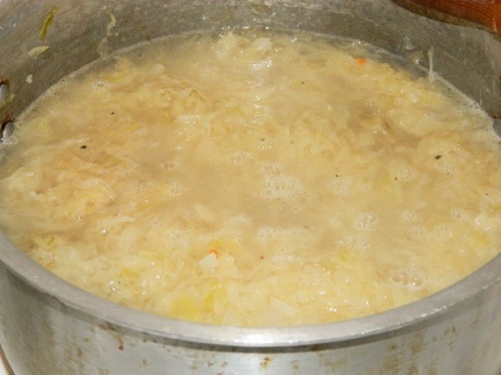 Boiling sauerkraut soup Adding cold water to the sauerkraut pot and bringing the rustic soup base to a gentle simmer.