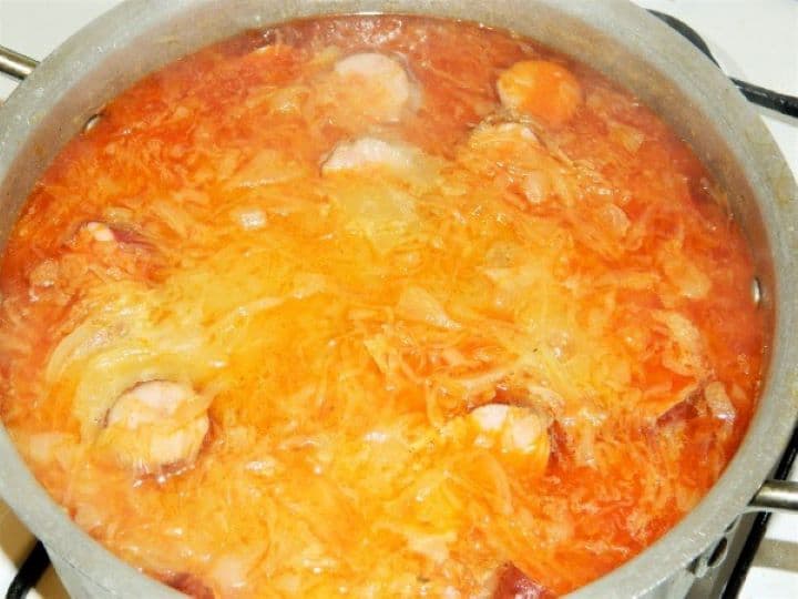 Sauerkraut sausage soup recipe ready Pouring the red paprika thickening roux paste through a fine mesh sieve directly into the bubbling sauerkraut soup.