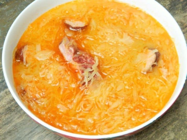 Sauerkraut sausage soup recipe A hot bowl of authentic Hungarian sauerkraut sausage soup, Korhelyleves, served in a rustic red bowl with fresh bread.
