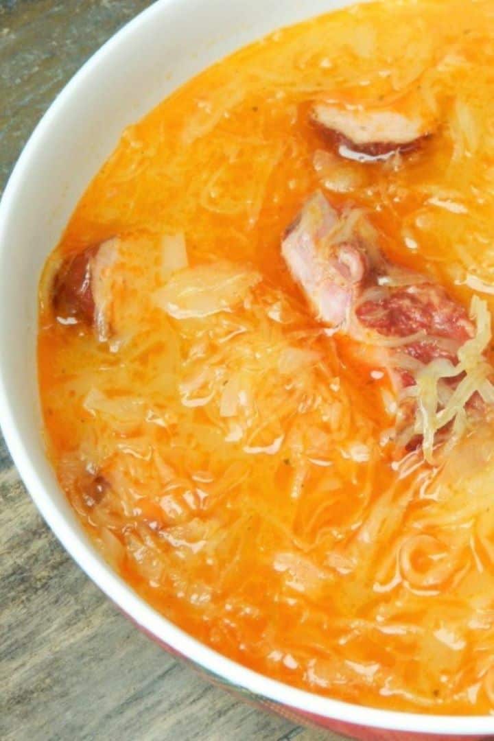 Transylvanian sauerkraut soup with smoked sausages and pork ribs plated in a white ceramic serving bowl.