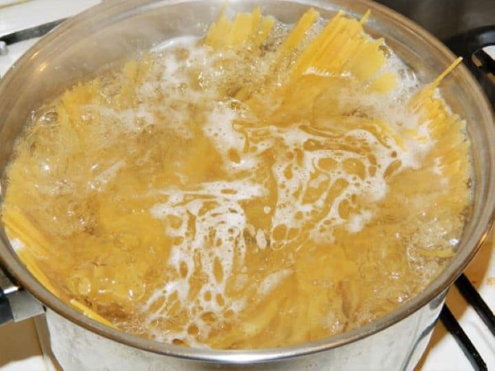 Boiling long spaghetti noodles in a large pot of hot salted water on the stovetop.
