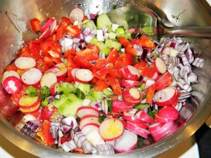 Finely diced cucumbers, red onions, radishes, and bell peppers mixed together in a large glass bowl.