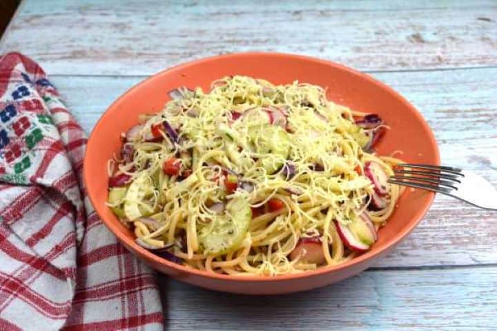 Close-up shot of cold vegetarian spaghetti salad showing sliced radishes, diced cucumbers, and fresh chives.