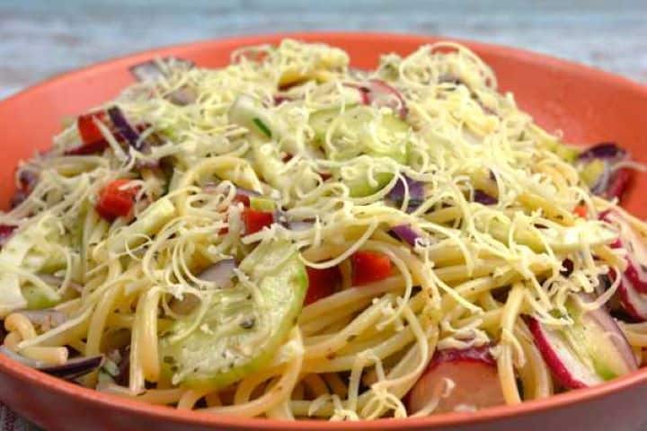 Close-up shot of vegetarian spaghetti salad showing sliced radishes, diced cucumbers, fresh chives, and grated cheddar.