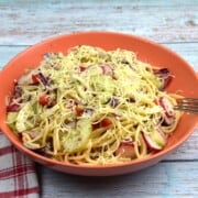 A refreshing bowl of vegetarian spaghetti salad mixed with crunchy vegetables and topped with shredded cheddar cheese.