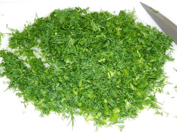 A bunch of aromatic fresh green dill finely minced on a kitchen chopping board.