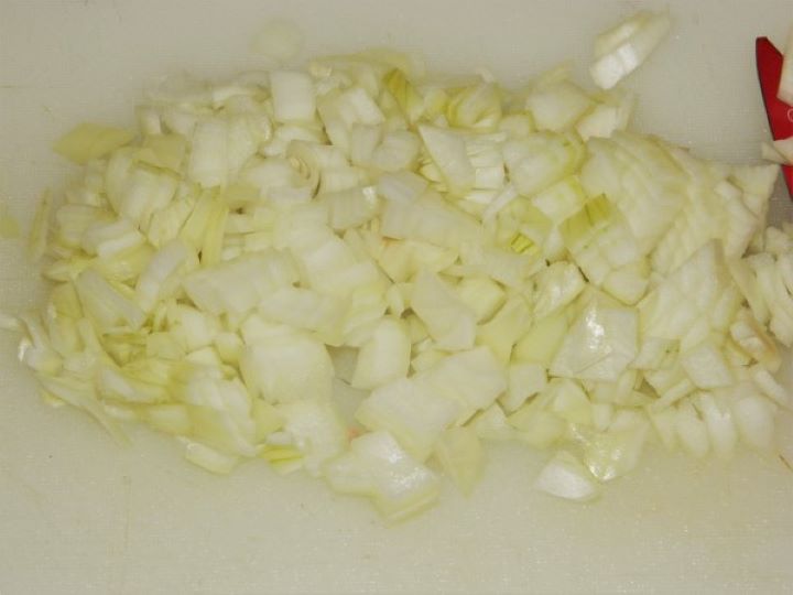 Finely chopped white onions on a white cutting board prepared as the savory base for a traditional soup.