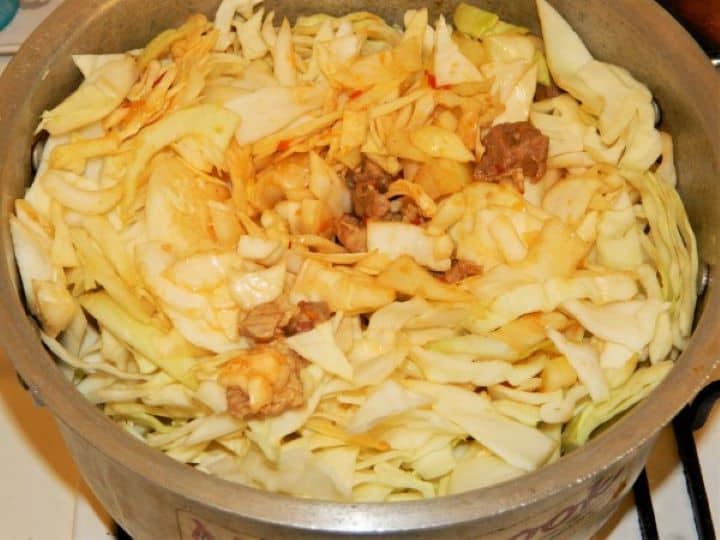 Adding finely shredded white cabbage ribbons and pouring smooth tomato passata into the soup pot with the pork.