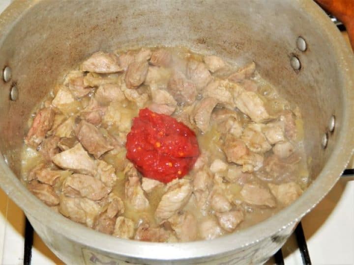Browning diced pork shoulder with sweet pepper paste and onions under a lid to create a flavorful stew base.