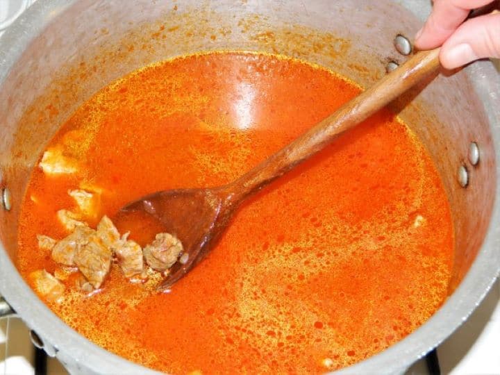 Simmering seasoned pork shoulder cubes in a shallow layer of warm water inside a covered pot.