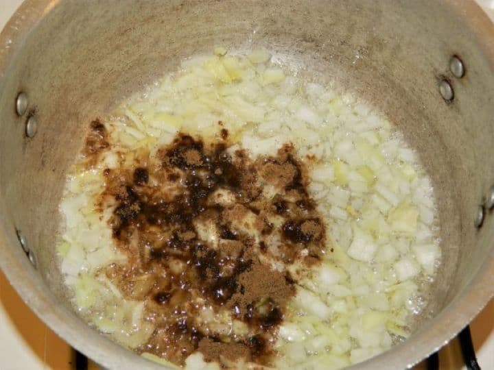 Sautéing chopped white onions seasoned with caraway powder, salt, and black pepper in a large soup pot.