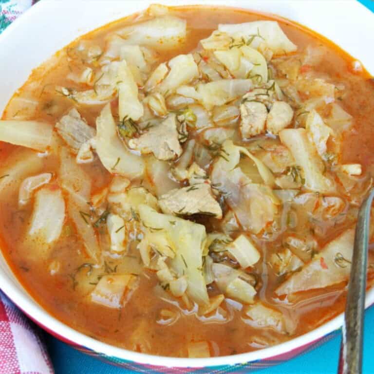 Traditional Hungarian cabbage soup called Lucskos Kaposzta served hot in a rustic ceramic bowl with sour cream and crusty bread.