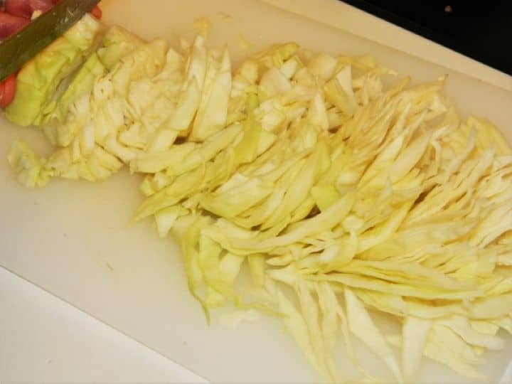 A large mound of fresh white cabbage shredded into very thin ribbons on a cutting board.