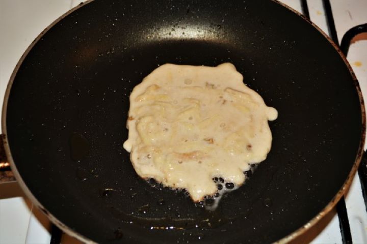 Easy Cinnamon Apple Pancakes Recipe-Frying Pancake on the First Side Frying a thick apple cinnamon pancake in a hot pan with sunflower oil, with the edges turned a crisp golden brown.