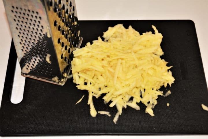 Easy Cinnamon Apple Pancakes Recipe-Grated Apples A box grater being used to shred fresh baking apples onto a cutting board for an easy cinnamon apple pancakes recipe.