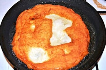 Deep-frying authentic Hungarian Langos in a pan until golden brown and bubbly