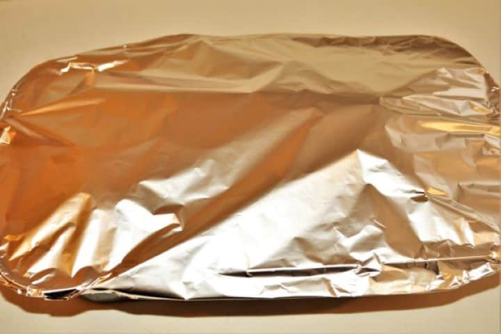 A loaf baking pan tightly covered with aluminum foil, ready to be placed in a preheated oven for baking.