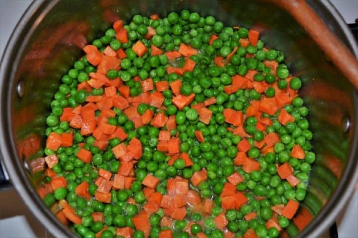 Sautéing frozen green peas and diced carrot cubes in sunflower oil in a large soup pot.