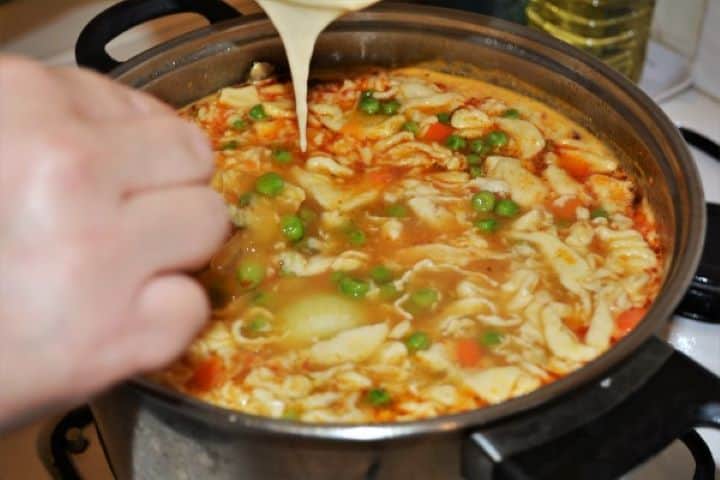 Using the wet fork method to drop rustic homemade egg noodles, galuska, into a simmering pot of Hungarian pea soup.