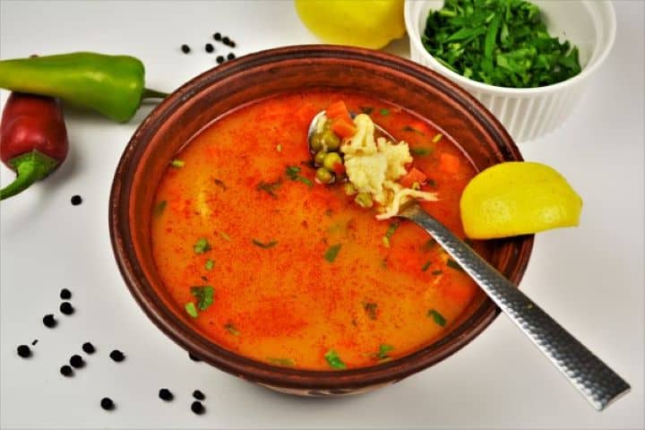 Close-up of a spoon lifting whole vibrant green peas and a tender homemade drop dumpling from a bowl of Hungarian Borsóleves.
