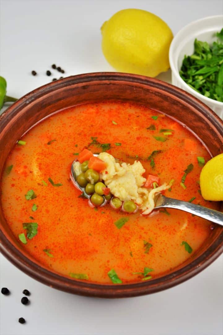A rustic bowl of authentic Hungarian green pea soup, Borsóleves, with clear paprika broth, whole sweet peas, carrots, and homemade drop dumplings garnished with fresh parsley.