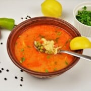 A rustic bowl of authentic Hungarian green pea soup, Borsóleves, with clear paprika broth, whole sweet peas, carrots, and homemade drop dumplings garnished with fresh parsley.