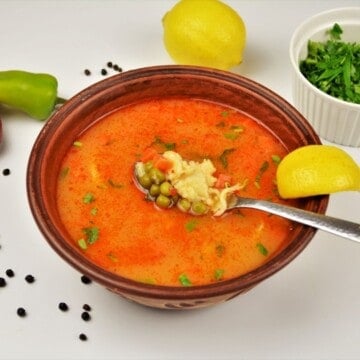A rustic bowl of authentic Hungarian green pea soup, Borsóleves, with clear paprika broth, whole sweet peas, carrots, and homemade drop dumplings garnished with fresh parsley.