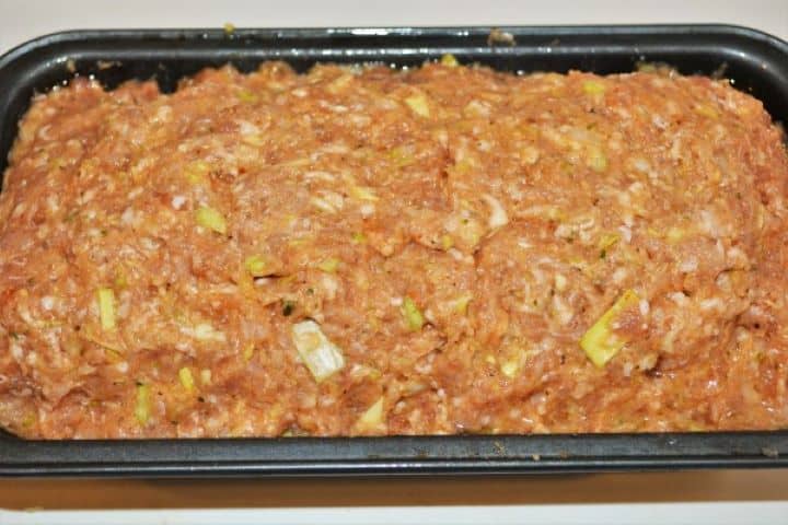 Smoothing the top layer of pork mince over the cheese and pepper filling in a loaf pan to seal the stuffing inside.