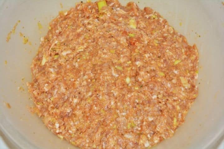 Mixing raw minced pork by hand in a bowl with eggs, soaked bread paste, sweet Hungarian paprika, and marjoram.