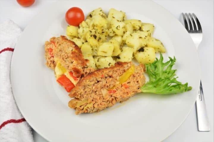 A plate of Hungarian stuffed meatloaf with cheese and peppers served alongside boiled parsley potatoes and cherry tomatoes.