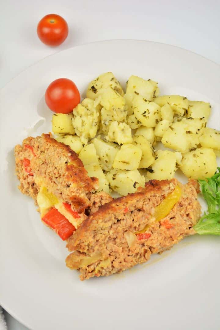 A close-up slice of juicy stuffed pork meatloaf showing a vibrant center of melted cheddar cheese, red kapia, and yellow bell peppers.