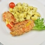 A close-up slice of juicy stuffed pork meatloaf showing a vibrant center of melted cheddar cheese, red kapia, and yellow bell peppers.