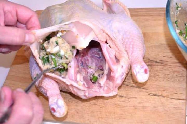 Baked Stuffed Whole Chicken Recipe-Filling the Chicken With Stuffing Spoon gently sliding the homemade bread filling through the neck opening and under the skin of a raw whole chicken.