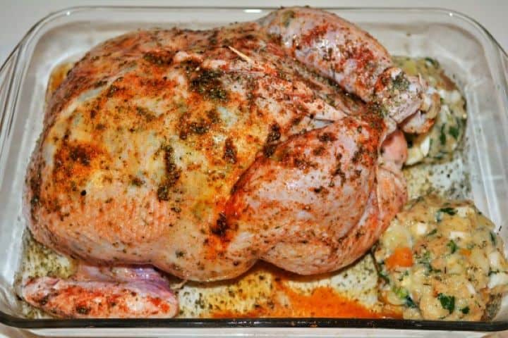 Baked Stuffed Whole Chicken Recipe-Seasoned Stuffed Chicken in the Tray Ready to Bake Uncooked stuffed whole chicken coated in oil and sweet Hungarian paprika inside a glass baking dish with two extra stuffing balls and beer.