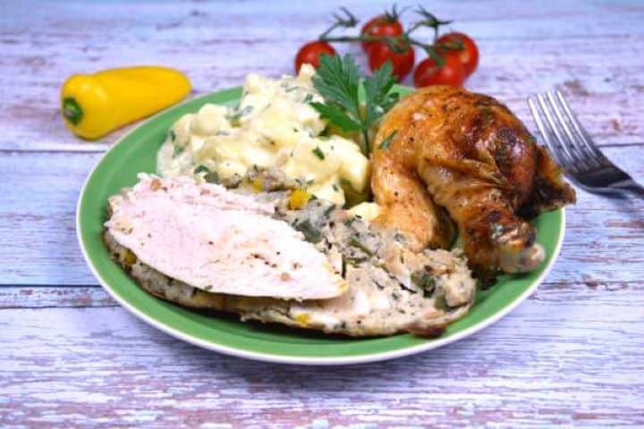 Baked Stuffed Whole Chicken Recipe-Served on Plate With Boiled Potatoes Slices of juicy roast chicken breast displaying a layer of savory bread stuffing directly underneath a crackling, crispy skin.