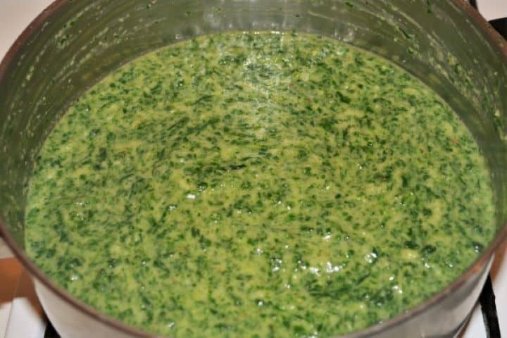 A close-up photograph of thick, velvety quick creamed spinach recipe, with visible pieces of garlic and chopped spinach in a pot.